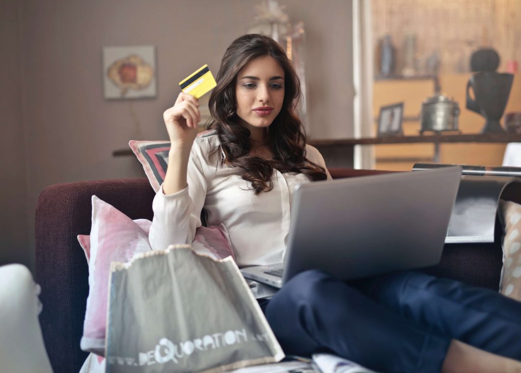 Woman holding credit card sitting on her laptop making purchases