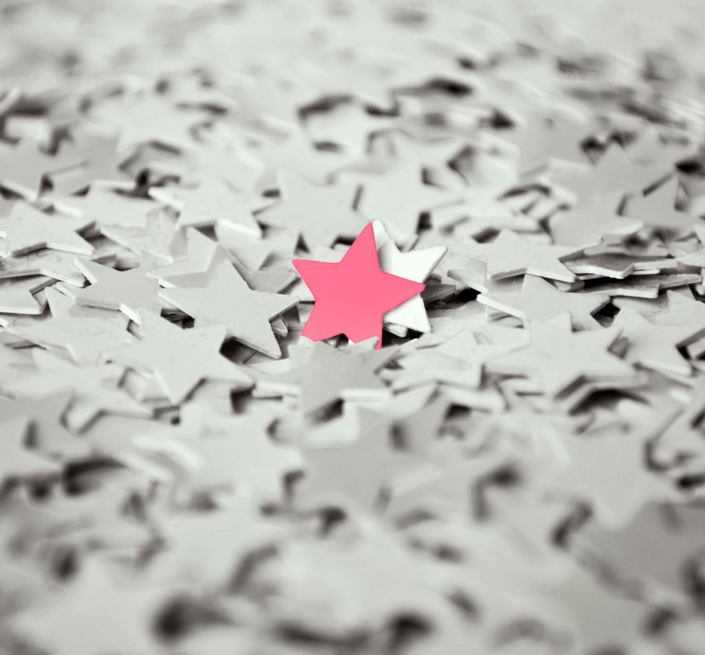 Pink paper star amongst a pile of white stars
