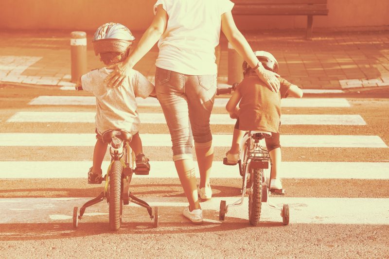 A parent with two children either side on trikes on a zebra crossing
