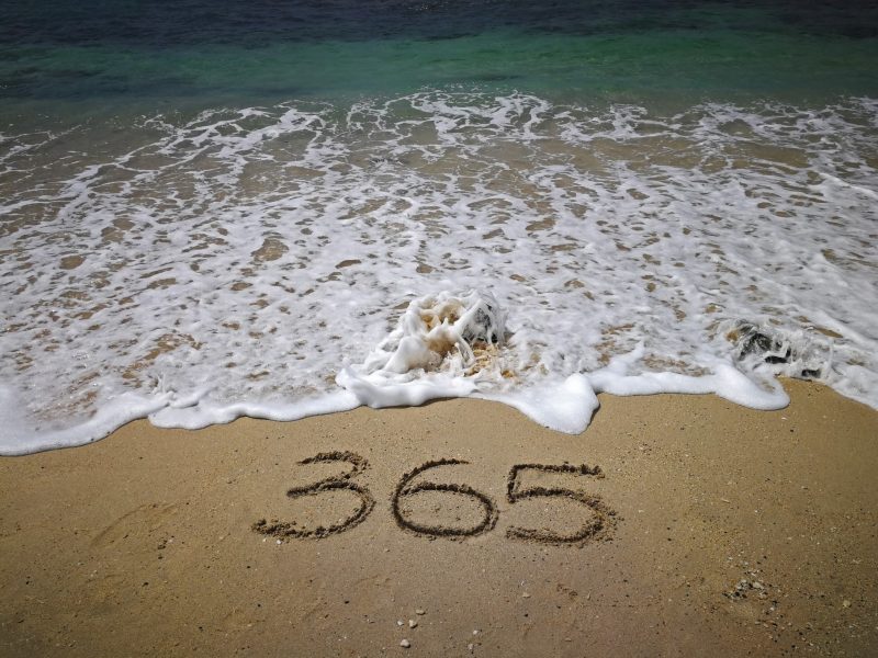 Beach with a wave coming in and the number 365 drawn in the sand