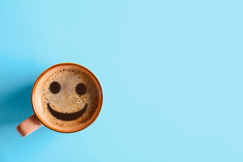 Coffee mug with a smiley face in the bubbles of a drink on a blue background.