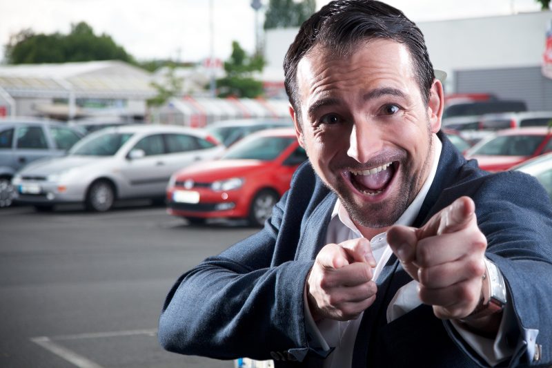 A used car salesman pointing at the camera and making cringy gestures to represent an inauthentic sales experience