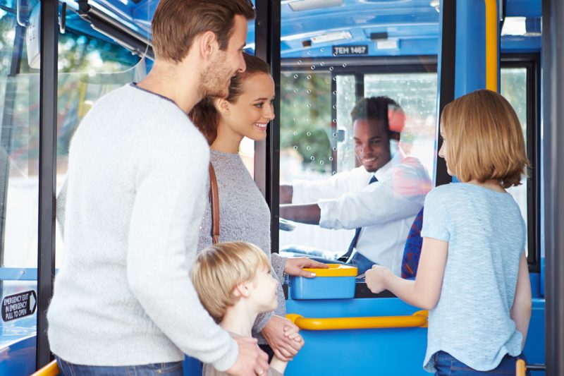 Family boarding a bus being greeted by a friendly driver